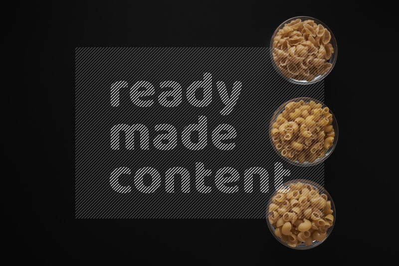 Different pasta types in 3 glass bowls on black background