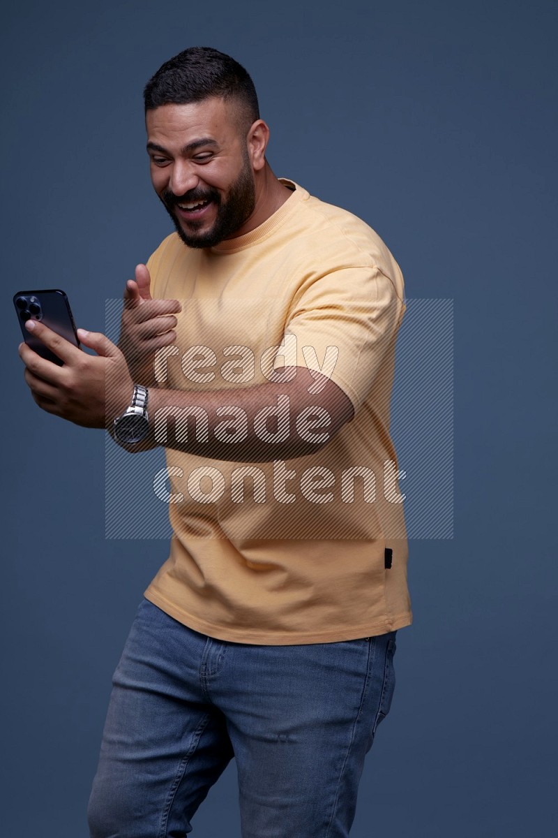 A man Pointing at a Smartphone on Blue Background wearing Orange T-shirt