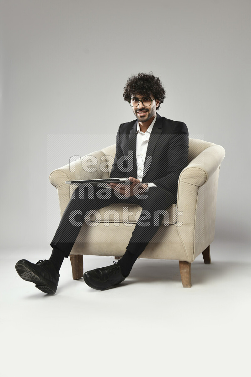 A man wearing formal sitting on a chair holding a laptop on white background