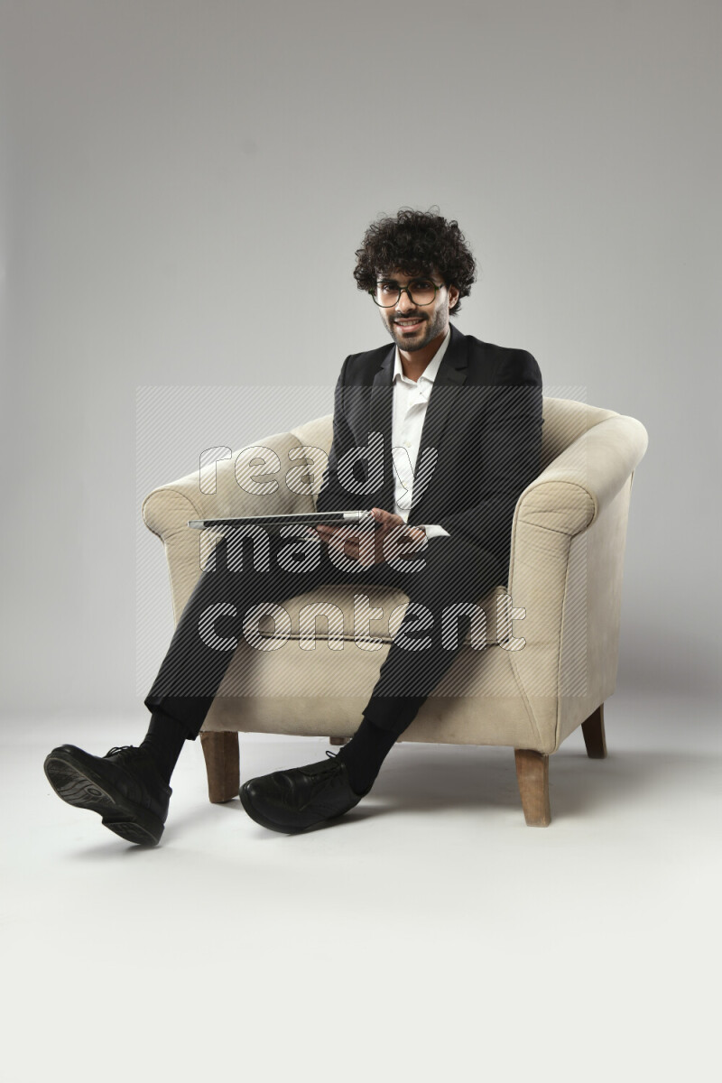 A man wearing formal sitting on a chair holding a laptop on white background