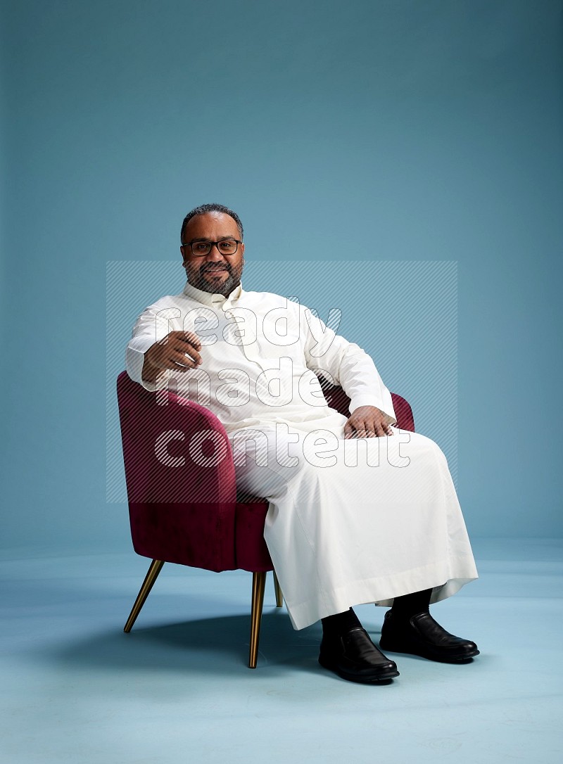 Saudi Man without shimag sitting on chair holding ATM card on blue background