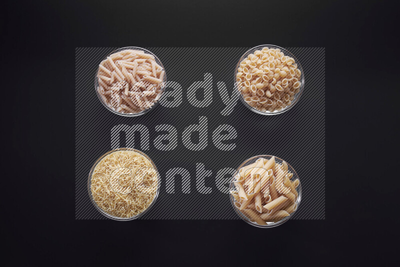 Different pasta types in glass bowls on black background