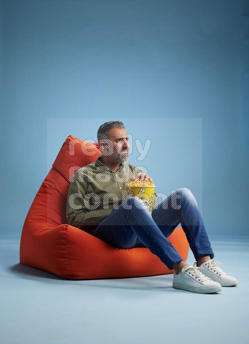 A man sitting on an orange beanbag and eating popcorn