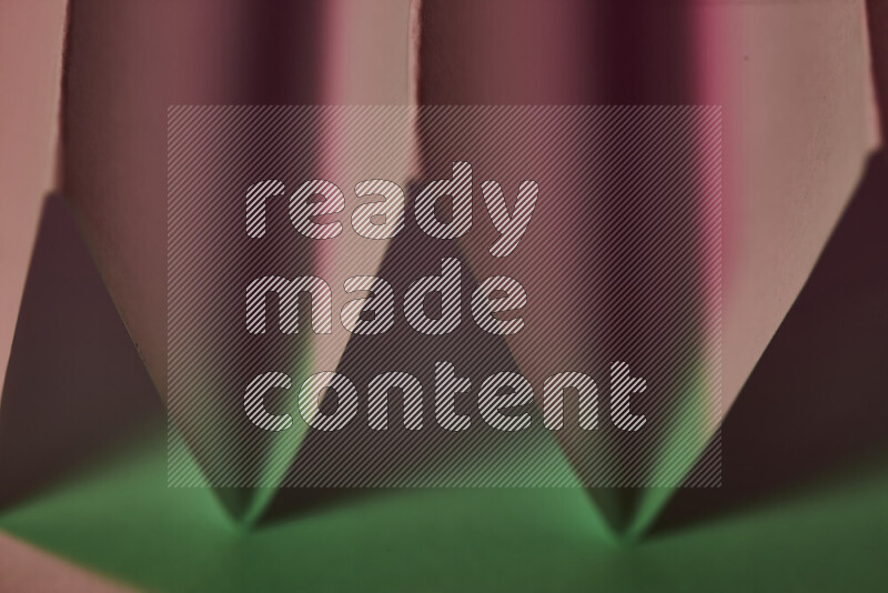 A close-up abstract image showing sharp geometric paper folds in green and pink gradients