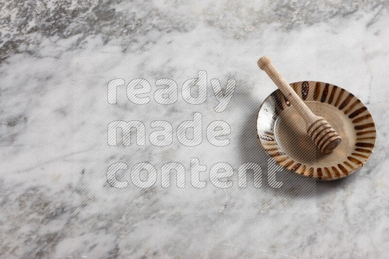 Multicolored pottery plate with wooden honey dipper in it on grey marble background