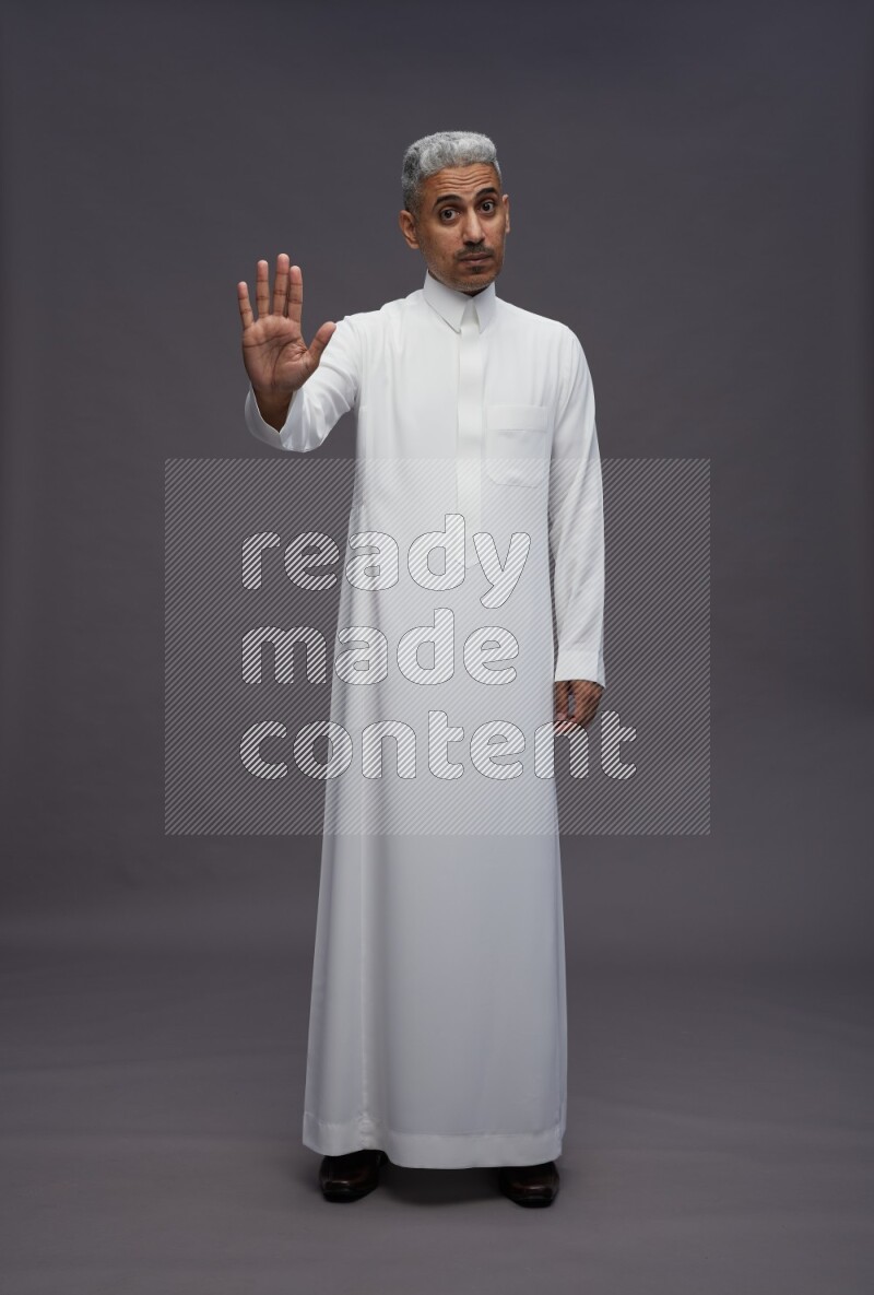 Saudi man wearing thob standing interacting with the camera on gray background