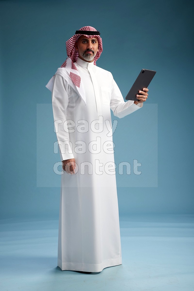 Saudi man wearing thob and shomagh with tablet on Blue background