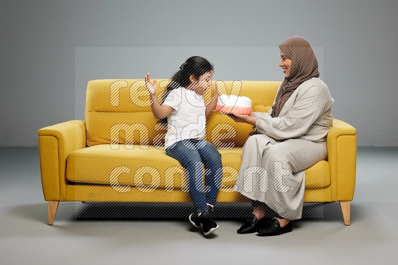 A girl sitting giving a cake to her mother on gray background