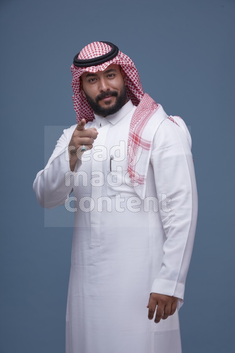 A Saudi man posing on blue background wearing Thob and Shomag