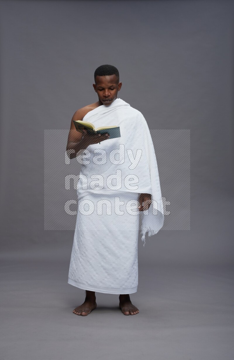 A man wearing Ehram Standing reading quran on gray background