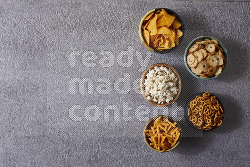 Assorted snacks in pottery bowls on grey background