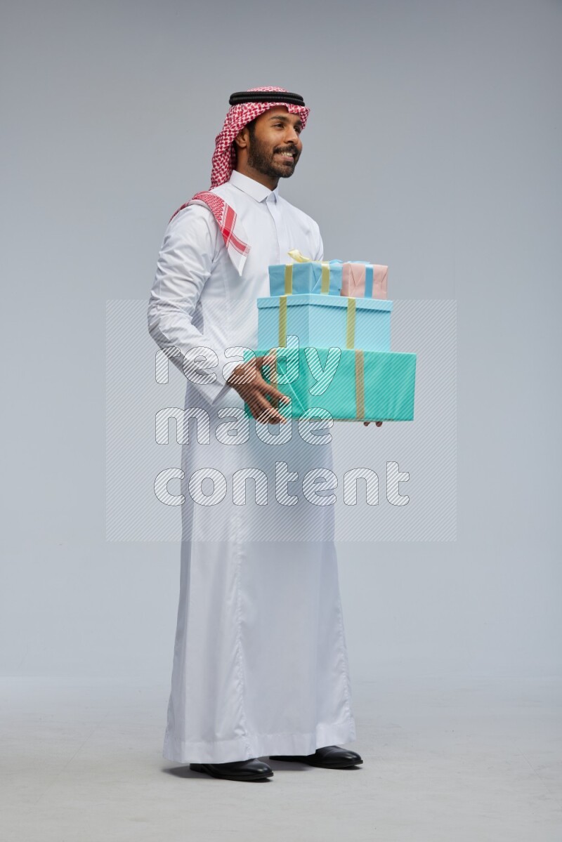 Saudi man Wearing Thob and shomag standing holding gift box on Gray background