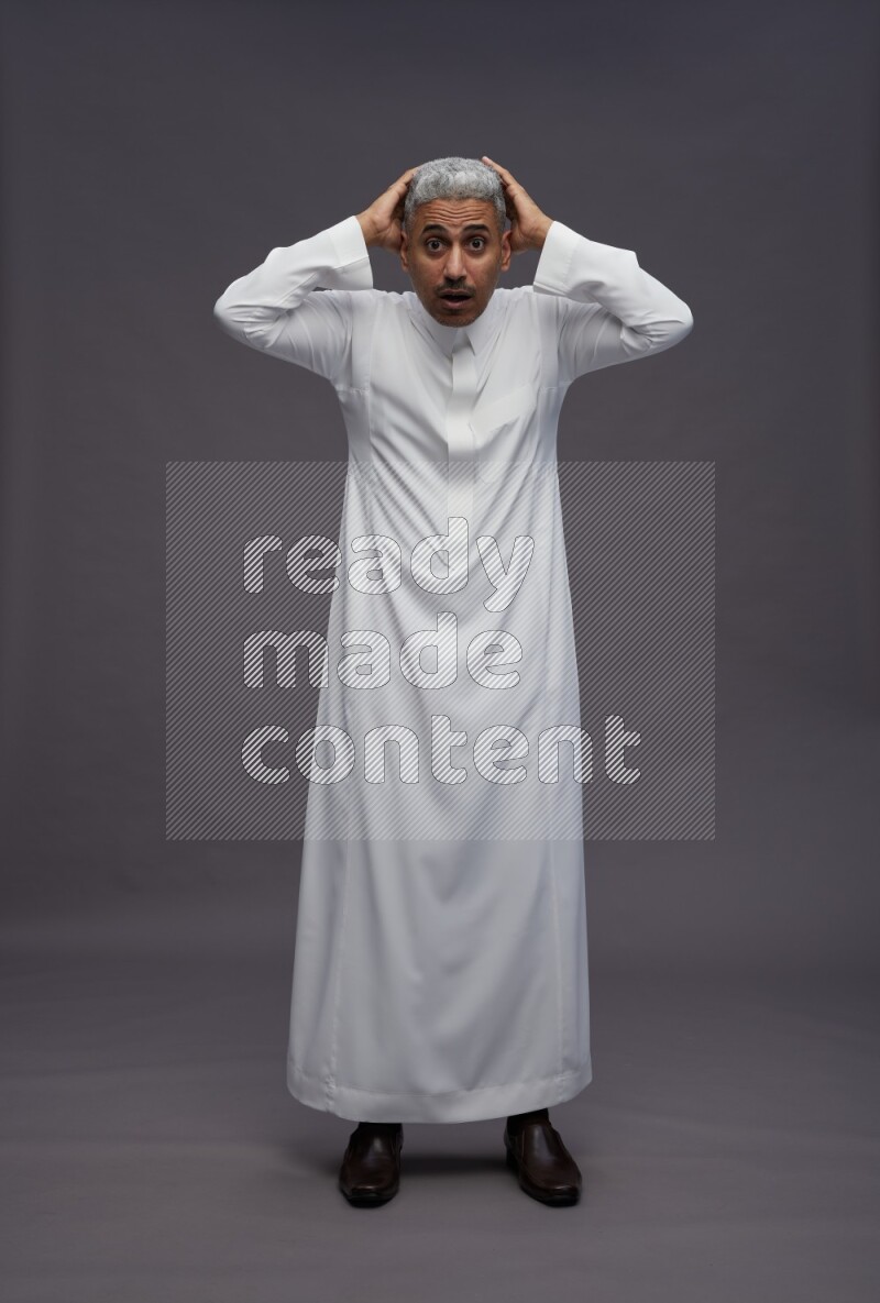Saudi man wearing thob standing hands behind head on gray background