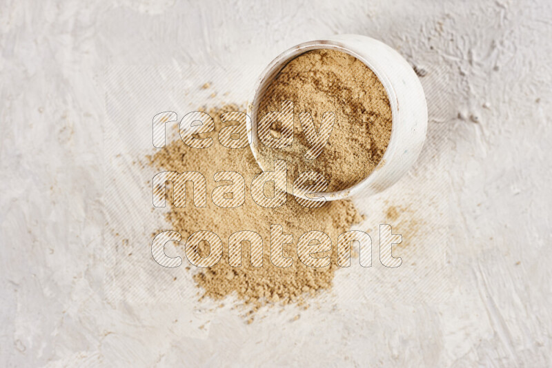 A beige pottery bowl full of ground ginger powder with fallen powder from it on white background