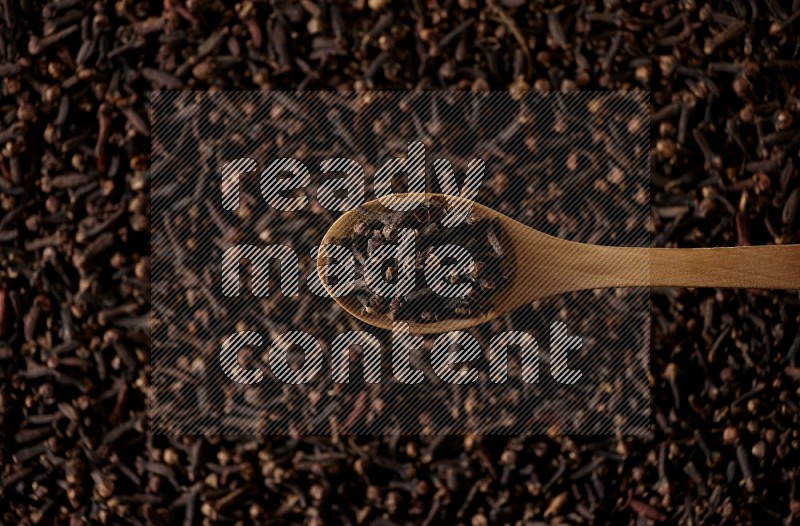 A wooden spoon full of cloves on cloves background and black flooring
