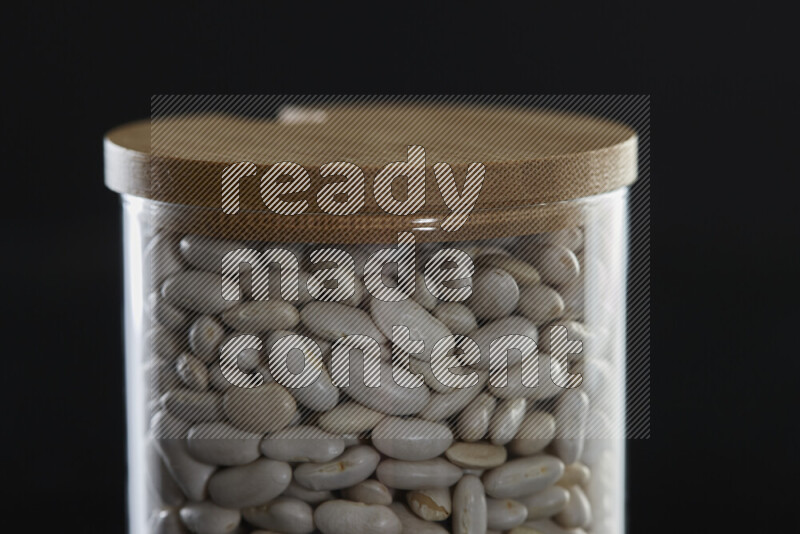 White beans in a glass jar on black background