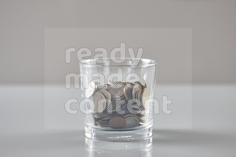 Random old coins in a glass cup on grey background