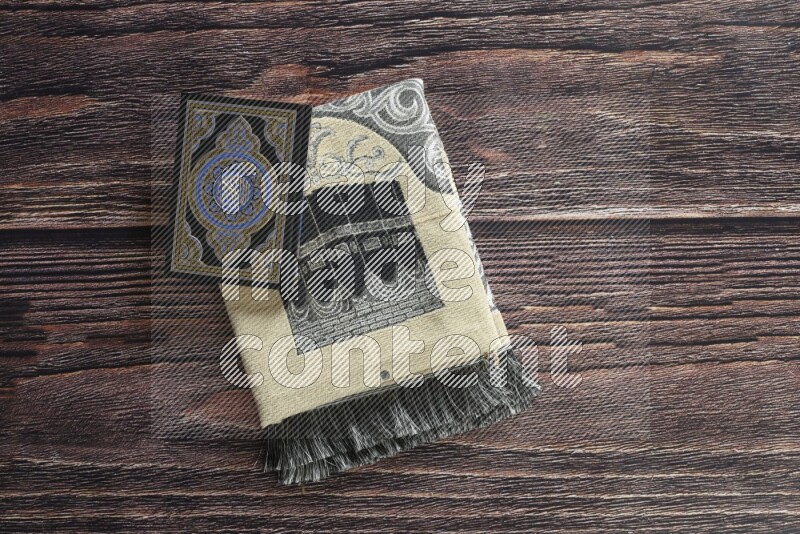 سجادة صلاة مطوية بعناصر مختلفة مثل القرآن الكريم وسبحة الصلاة على خلفية خشبية بنية