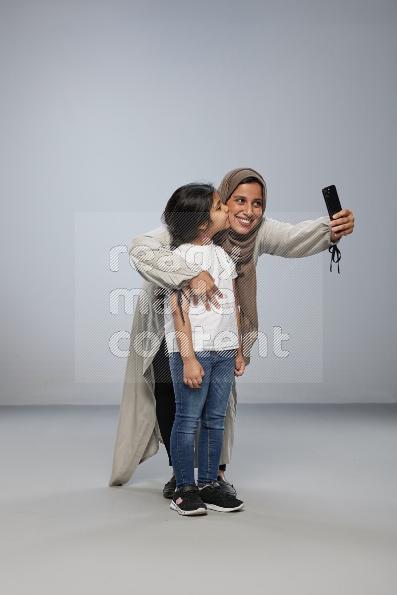 A girl standing taking selfie with her mother on gray background