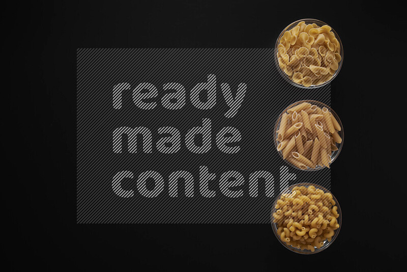 Different pasta types in 3 glass bowls on black background