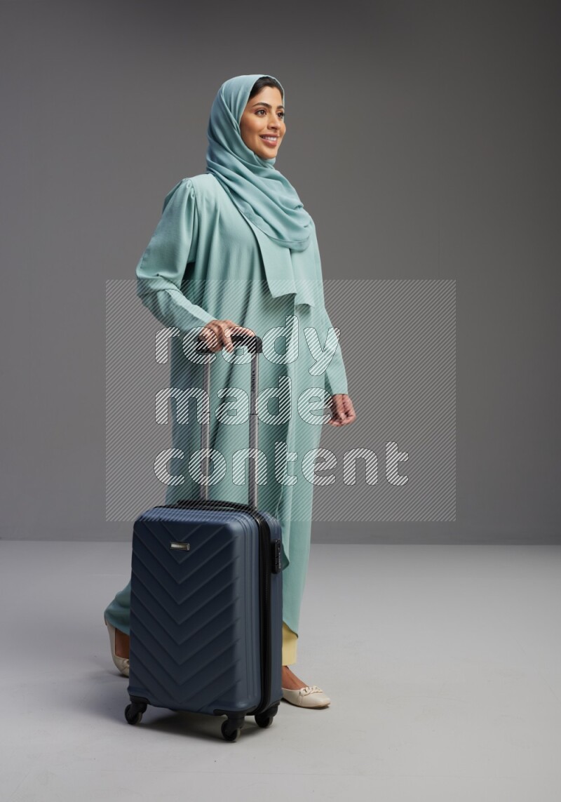 Saudi Woman wearing Abaya standing holding Travel bag on Gray background