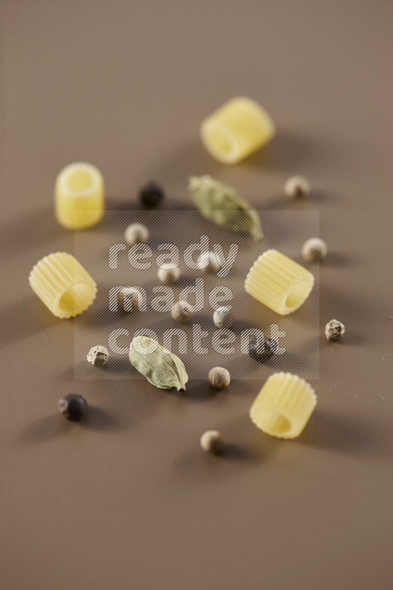 Raw pasta with different ingredients such as cherry tomatoes, garlic, onions, red chilis, black pepper, white pepper, bay laurel leaves, rosemary and cardamom on beige background