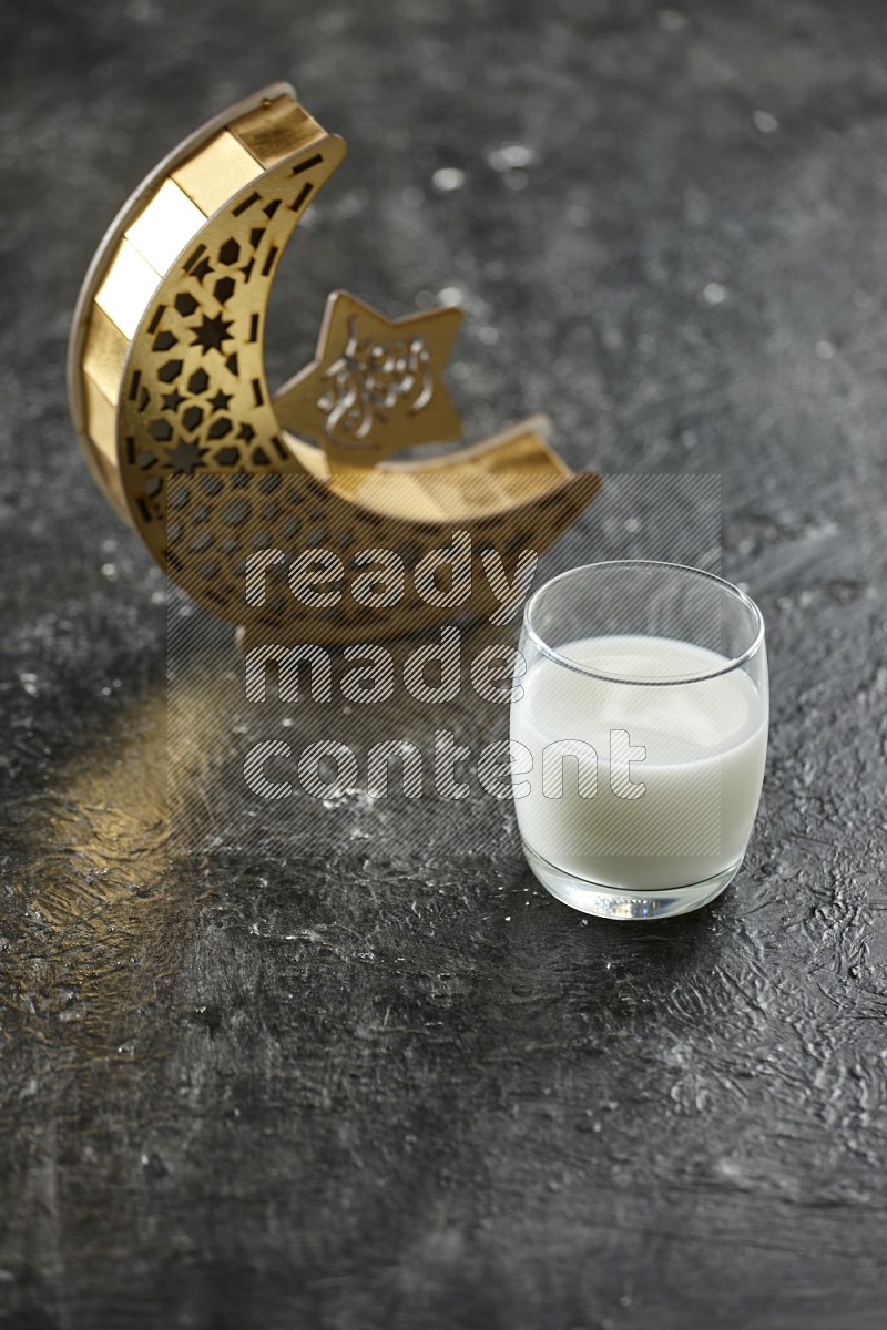 A wooden golden crescent lantern with different drinks, dates, nuts, prayer beads and quran on textured black background