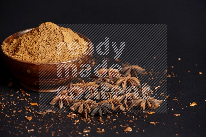 Star Anise powder in a wooden bowl with star anise beside it on a black background