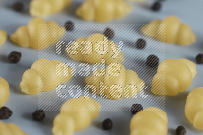 Raw pasta with different ingredients such as cherry tomatoes, garlic, onions, red chilis, black pepper, white pepper, bay laurel leaves, rosemary, cardamom and mushrooms on light blue background