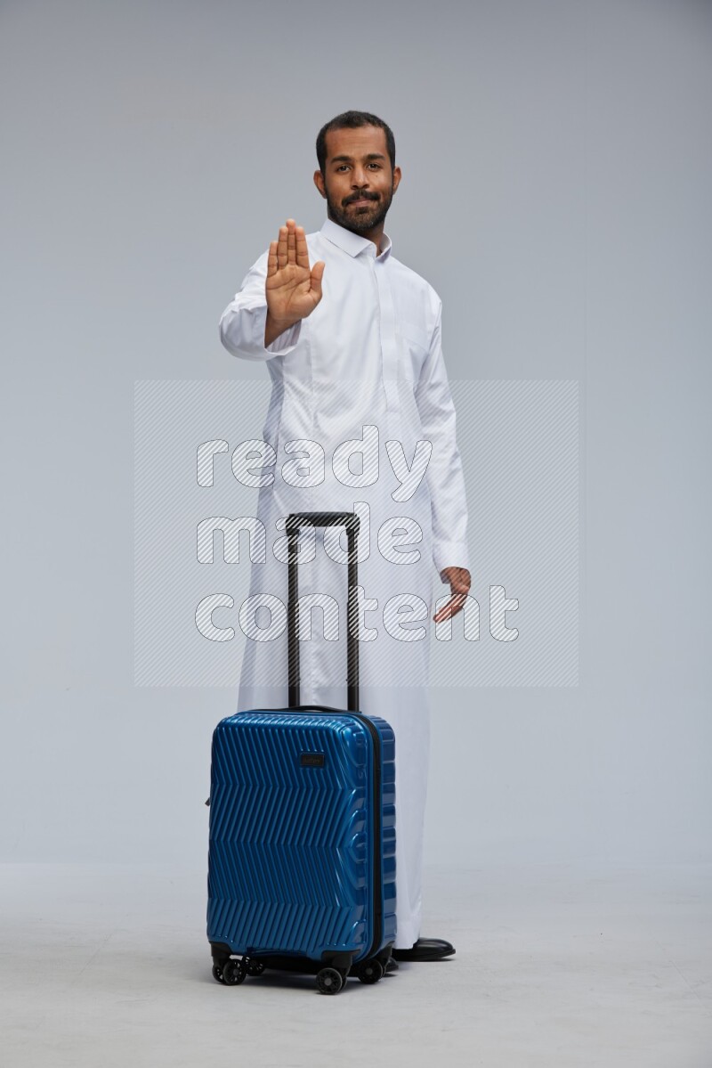 Saudi man wearing thob standing holding Travel bag on Gray background