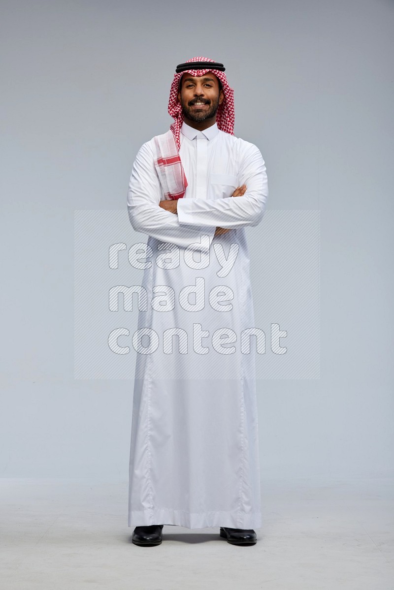 Saudi man Wearing Thob and shomag standing with crossed arms on Gray background