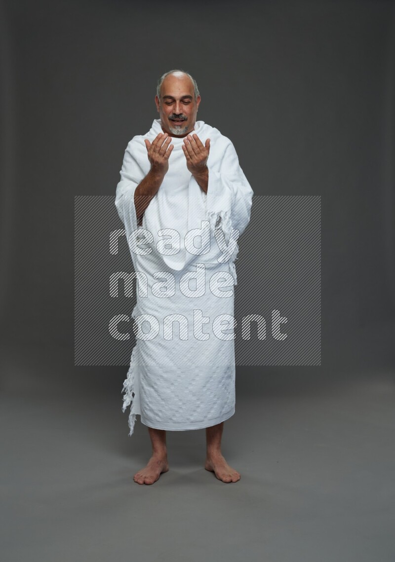 A man wearing Ehram Standing dua'a on gray background