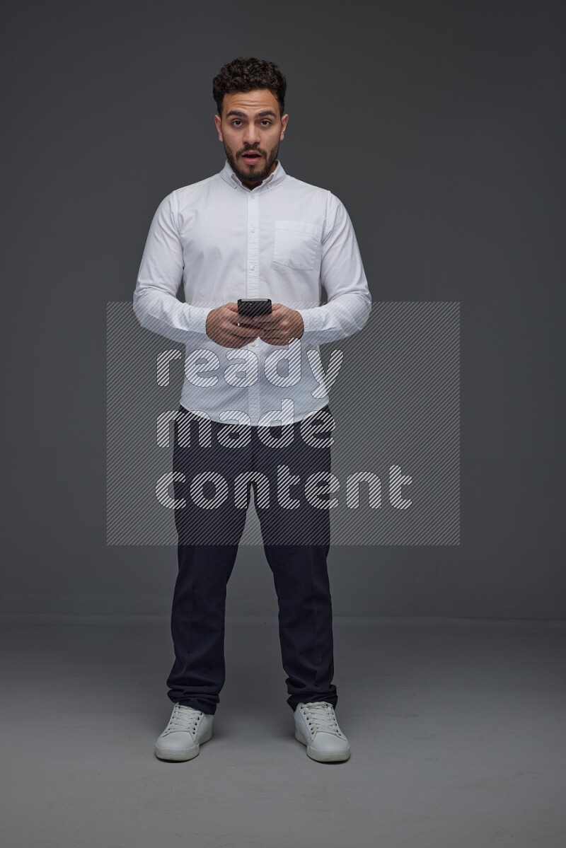 A man wearing smart casual standing and using his phone eye level on a gray background