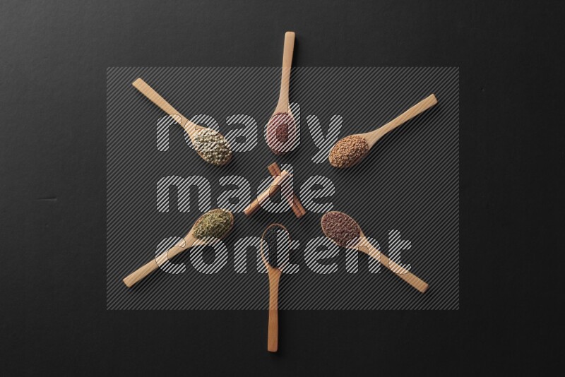 wooden spoons filled with white peppers, mustard seeds, black seeds, garden cress, cumin and flax on black flooring and shaped like a clock