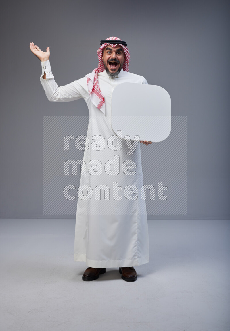 Saudi man Wearing Thob and red Shomag standing holding social media sign on Gray background