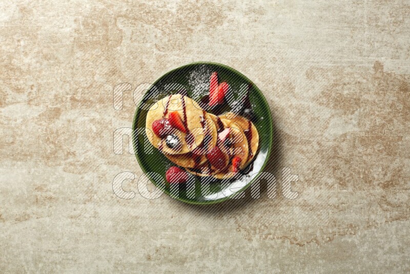 Five stacked mixed berries mini pancakes in a green plate on beige background