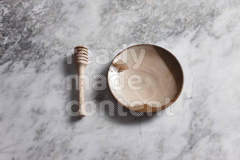 Multicolored pottery plate with wooden honey dipper on the side on grey marble background