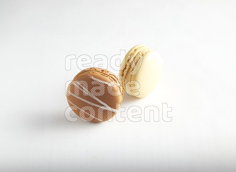 45º Shot of of two assorted Brown Irish Cream, and Yellow Vanilla macarons on white background