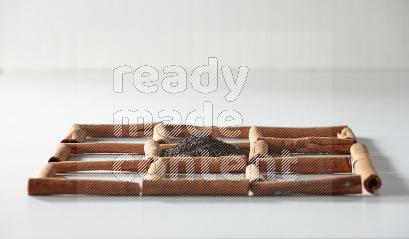 9 squares of cinnamon sticks full of tea in the middle surrounded by nutmeg, dried mint, cloves, dried basil, dried ginger, cinnamon, star anise and cardamom on white flooring