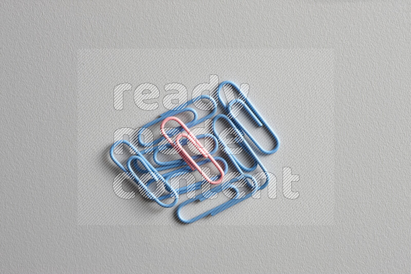 A pink paperclip surrounded by bunch of blue paperclips on grey background