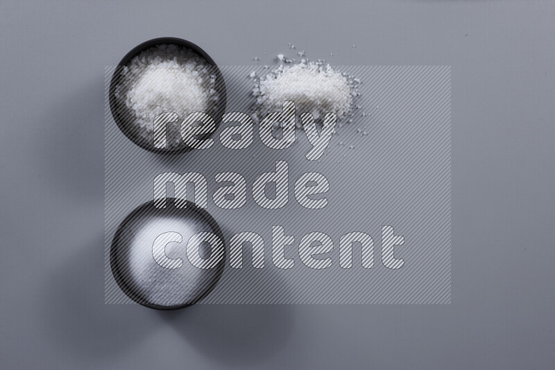 2 وعاء فخاري احدهمها ممتلئ بملح الطعام الأبيض والأخر بملح البحر الخشن على خلفية رمادية