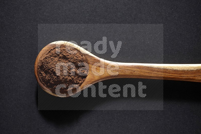 A wooden ladle full of cloves powder on a black flooring