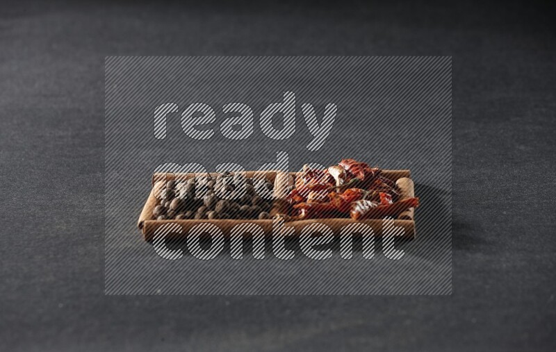 مربعان من أعواد القرفة ممتلئان بالفلفل الحار المجفف وحبوب بهار الفلفل الحلو علي خلفية سوداء