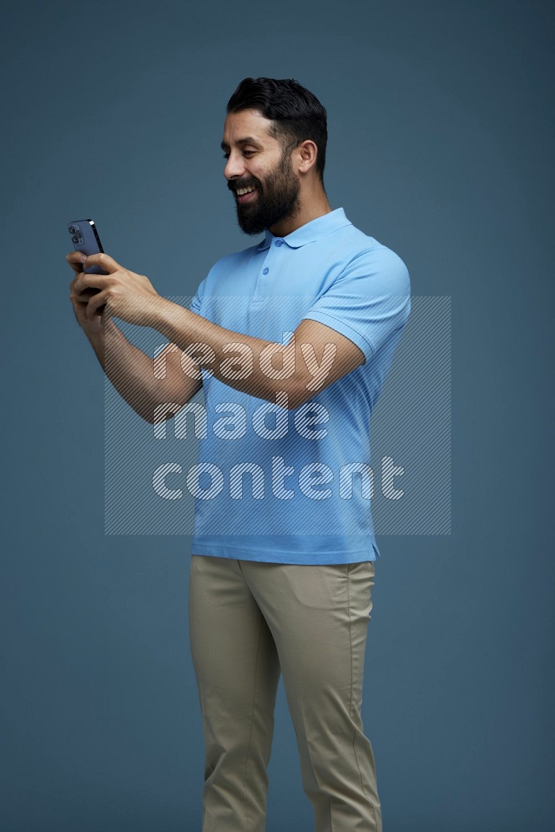 A man Texting on his phone in a blue background wearing a Blue shirt