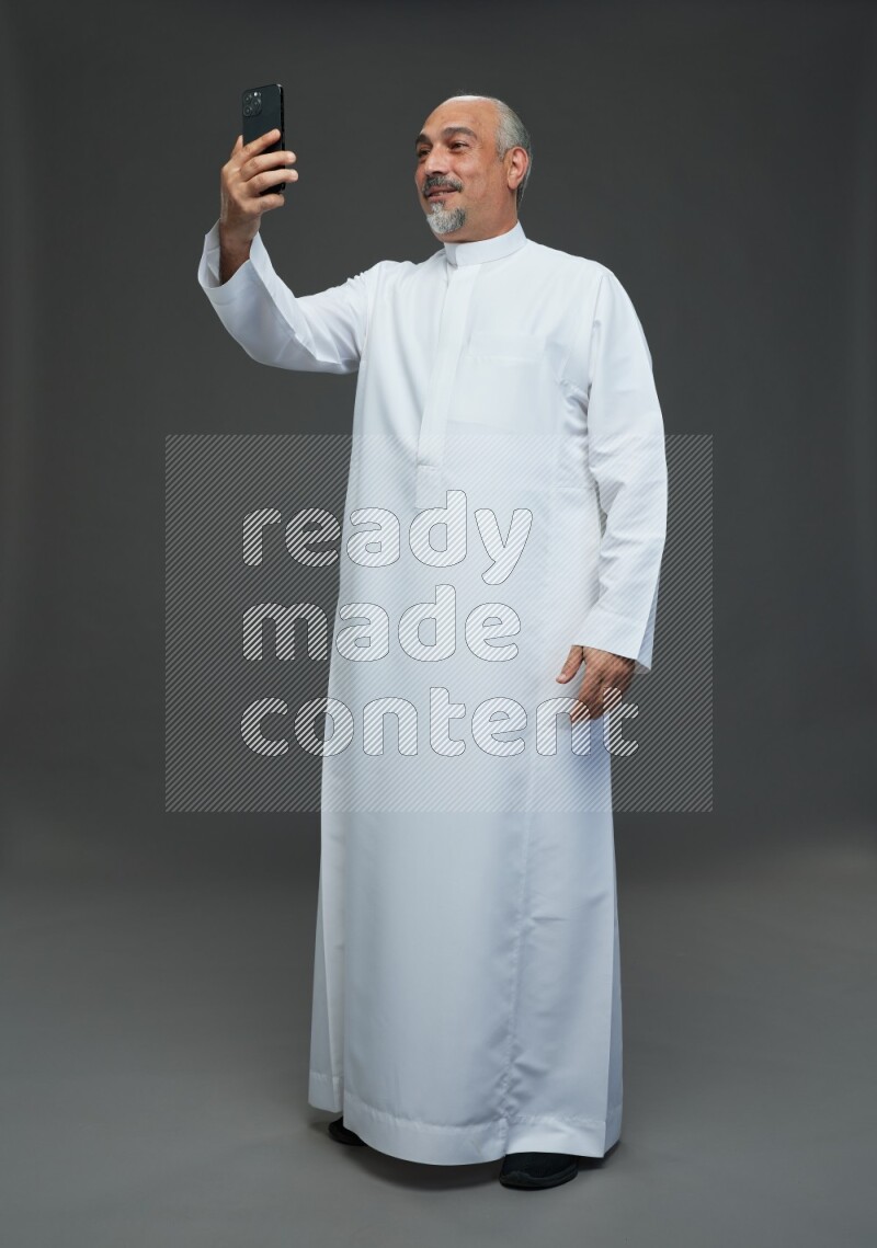 Saudi man without shomag Standing taking selfie on gray background