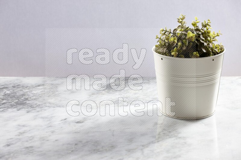 Green artificial plant in white pot on light grey marble background