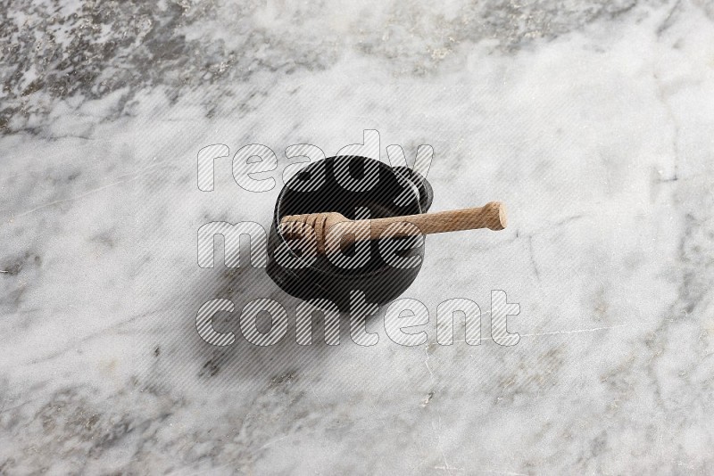 Black Pottery Bowl with wooden honey handle in it, on grey marble flooring, 65 degree angle