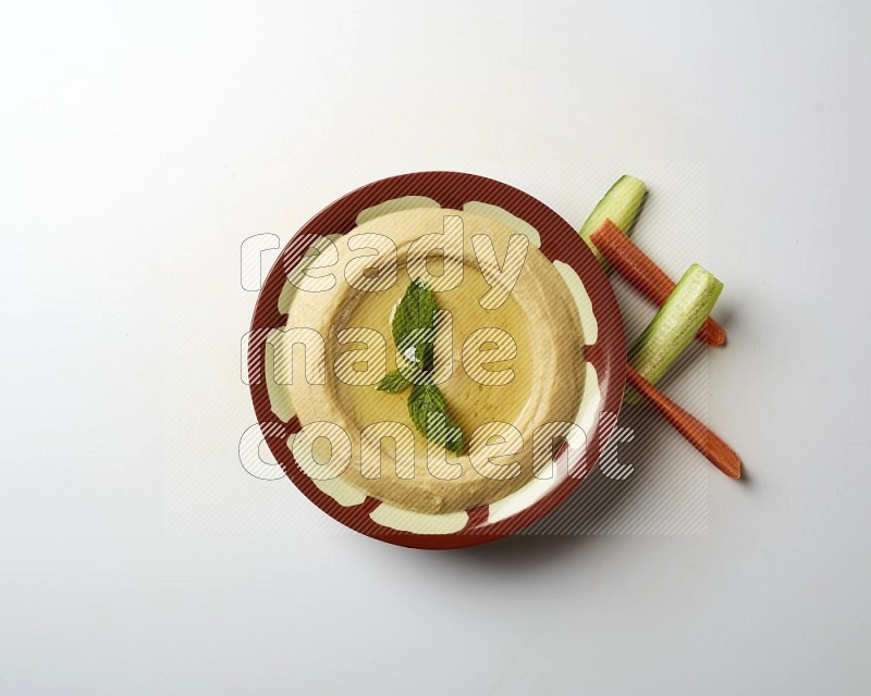 Hummus in a traditional plate garnished with mint on a white background