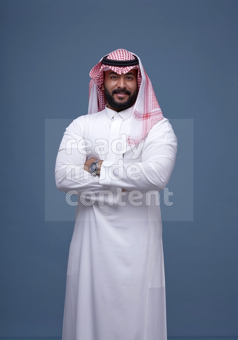 A Saudi man posing on blue background wearing Thob and Shomag