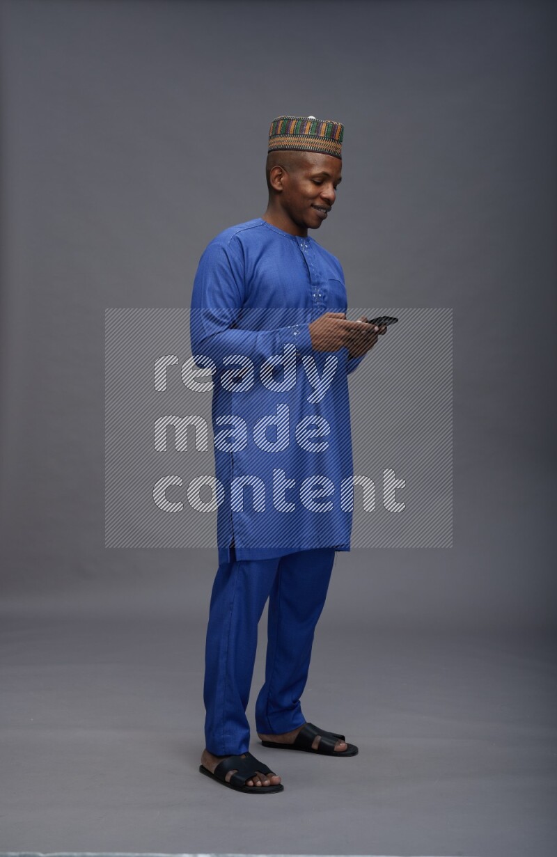 Man wearing Nigerian outfit standing texting on phone on gray background